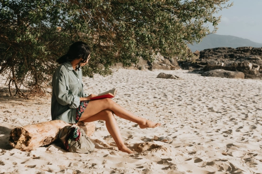 person-reads-their-novel-sitting-on-a-sandy-beach
